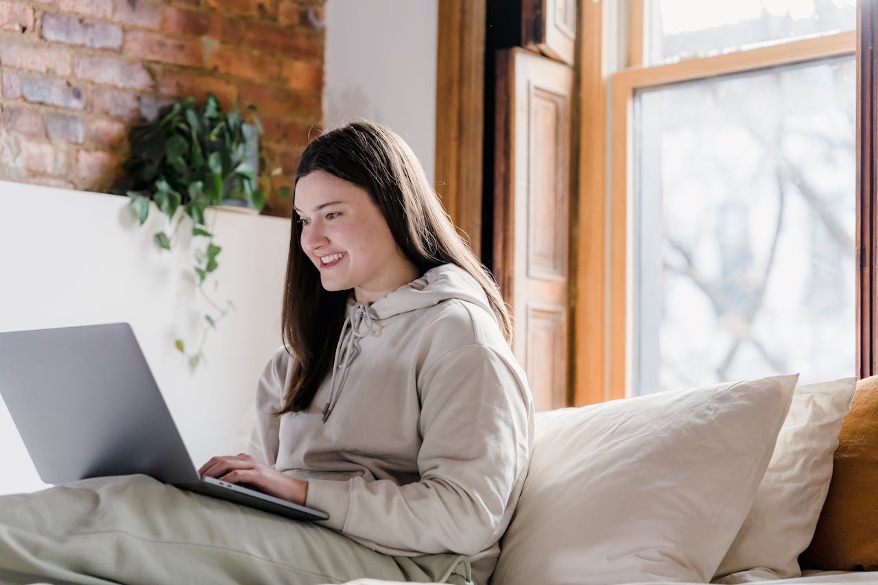 Positive woman browsing laptop in bedroom during remote work